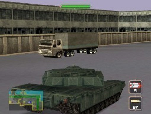 Ein grüner Panzer steht vor einem Lastwagen mit grauem Anhänger und einem großen Gebäude im Hintergrund.
