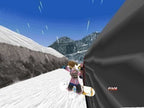 Eine Snowboarderin fährt nah an einer dunklen Felswand entlang, im Hintergrund weitere Berge.