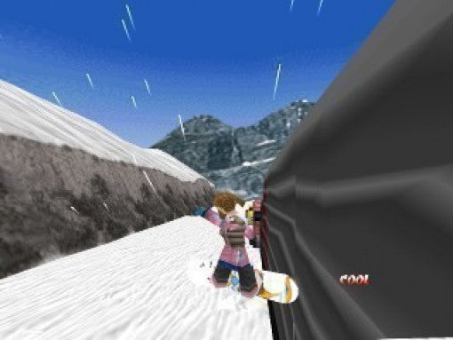 Eine Snowboarderin fährt nah an einer dunklen Felswand entlang, im Hintergrund weitere Berge.