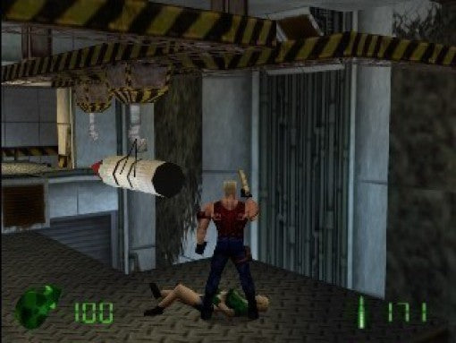 Duke Nukem steht mit einer Waffe über einer am Boden liegenden Frau, während eine Rakete von der Decke hängt.