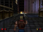 Duke Nukem steht in einer dunklen Stadtgasse und schießt auf einen Gegner, der in der Ferne explodiert.