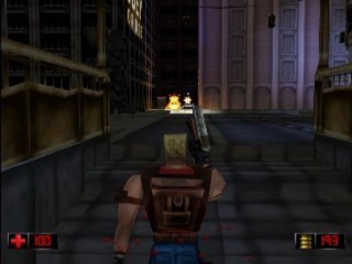 Duke Nukem steht in einer dunklen Stadtgasse und schießt auf einen Gegner, der in der Ferne explodiert.