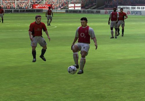 Ein Fussballspieler in rotem Trikot dribbelt den Ball auf dem grünen Rasen, weitere Spieler im Hintergrund.