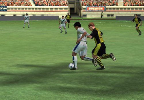 Zwei Fußballspieler kämpfen auf dem Rasen um den Ball, im Hintergrund sind weitere Spieler und ein Stadion zu sehen.