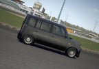 Ein schwarzer Kombi fährt auf einer Rennstrecke, im Hintergrund sind Tribünen und Gebäude zu sehen.