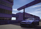 Ein blauer Sportwagen steht im Paddock des Tsukuba Circuits vor den Gebäuden der Rennstrecke.