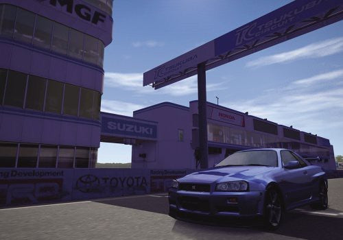 Ein blauer Sportwagen steht im Paddock des Tsukuba Circuits vor den Gebäuden der Rennstrecke.