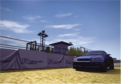 Ein blauer Sportwagen steht auf einer Rennstrecke neben einer Wand mit dem Tsukuba Circuit Logo.