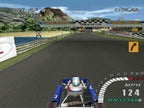 Ein Kart fährt auf einer Rennstrecke mit einer Start-Ziel-Brücke und Zuschauertribünen.