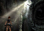 Lara Croft steht in einer dunklen Höhle, ein Lichtstrahl fällt von oben herein.