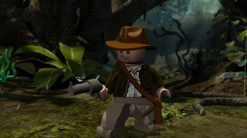 LEGO Indiana Jones steht mit einer Pistole in der Hand in einem dichten Dschungel.