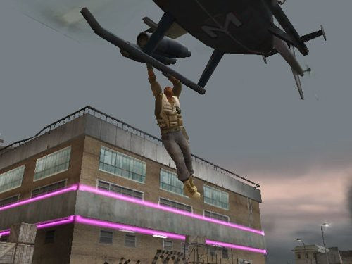 Ein Mann hängt an der Kufe eines Helikopters, der über einem Gebäude fliegt.