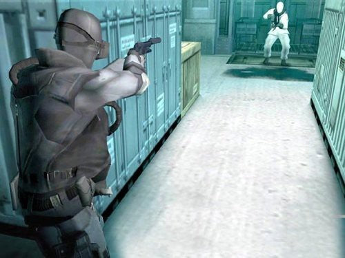 Solid Snake zielt mit einer Pistole auf einen einzelnen Gegner in einem weißen Anzug in einem engen Gang voller Container.