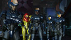 Samus Aran in ihrem gelb-roten Anzug steht zusammen mit vier Soldaten in blauen Rüstungen in einem futuristischen Raum.