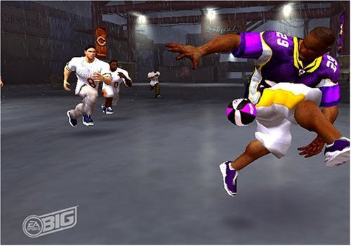 Ein American-Football-Spieler in lila-gelbem Trikot dribbelt den Ball in einer Halle, weitere Spieler im Hintergrund.