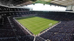 Eine weite Ansicht eines leeren Fußballstadions mit grüner Rasenfläche und Zuschauerrängen.